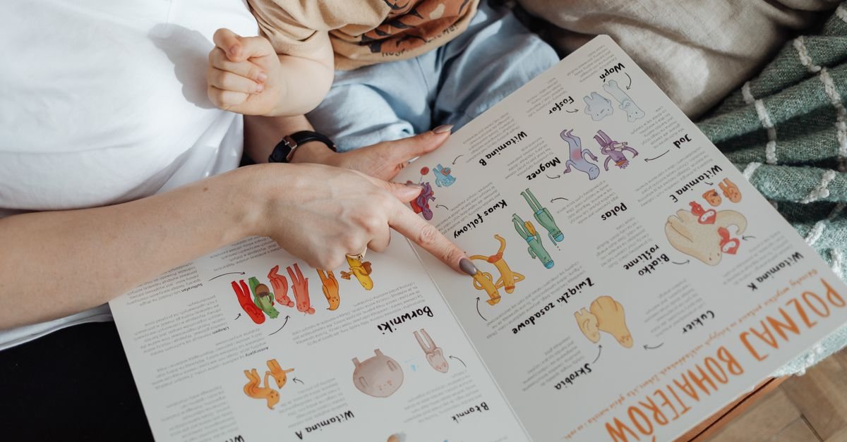 ソファで子どもを抱きながら、大人が絵本の絵を指さしている手元。ことばの手前にある指さしのやりとりのイメージ