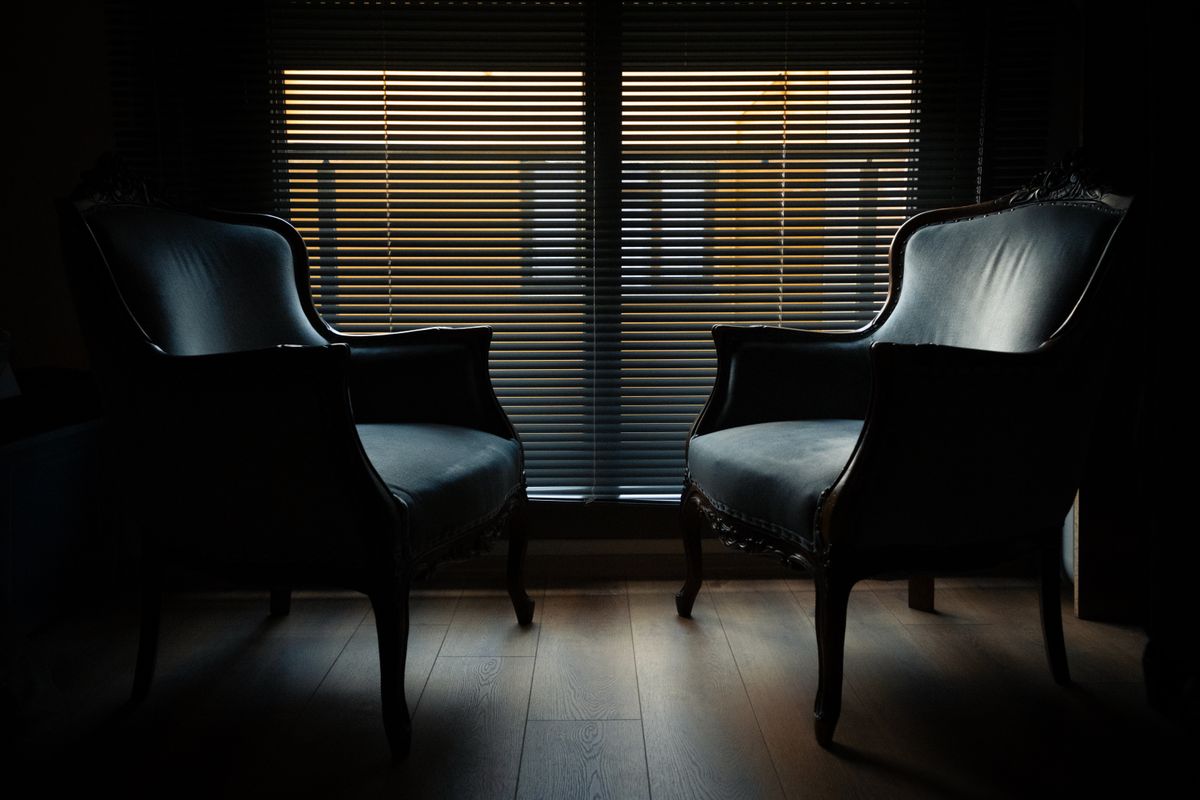 夜の部屋で窓のブラインドの光を背に並ぶ2脚のいす。同じ家にいても話が届かないまま向き合えずにいる時間のイメージ