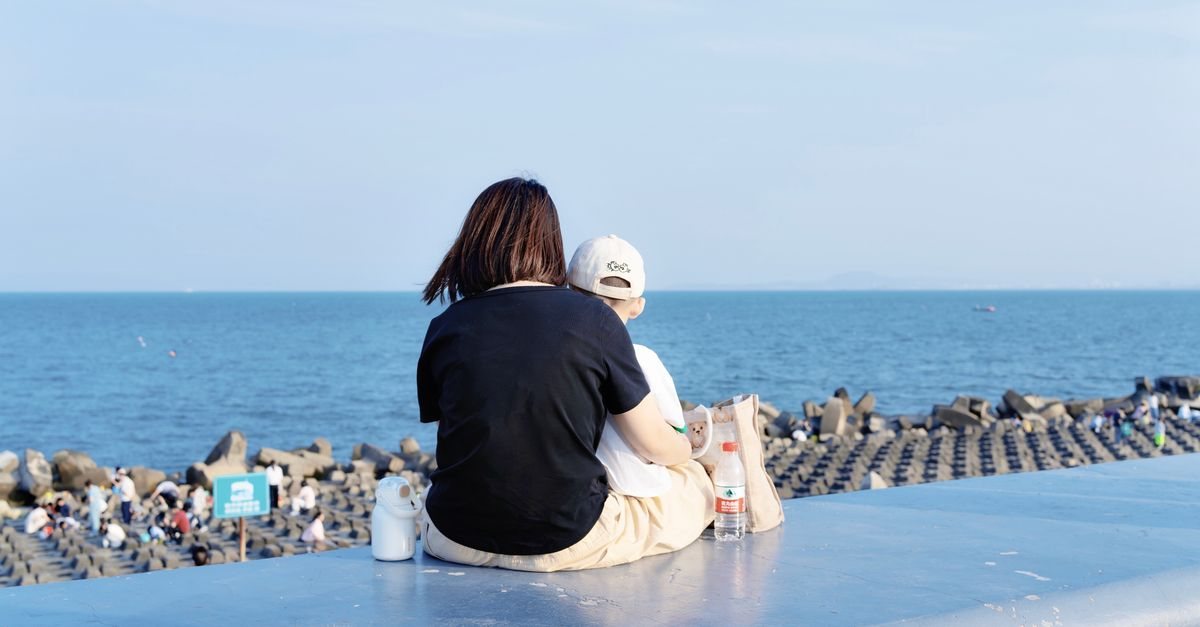 海辺の堤防に並んで座り、海をながめる母親と子どもの後ろ姿。子どもに特性のことをどう話そうか考えている場面のイメージ