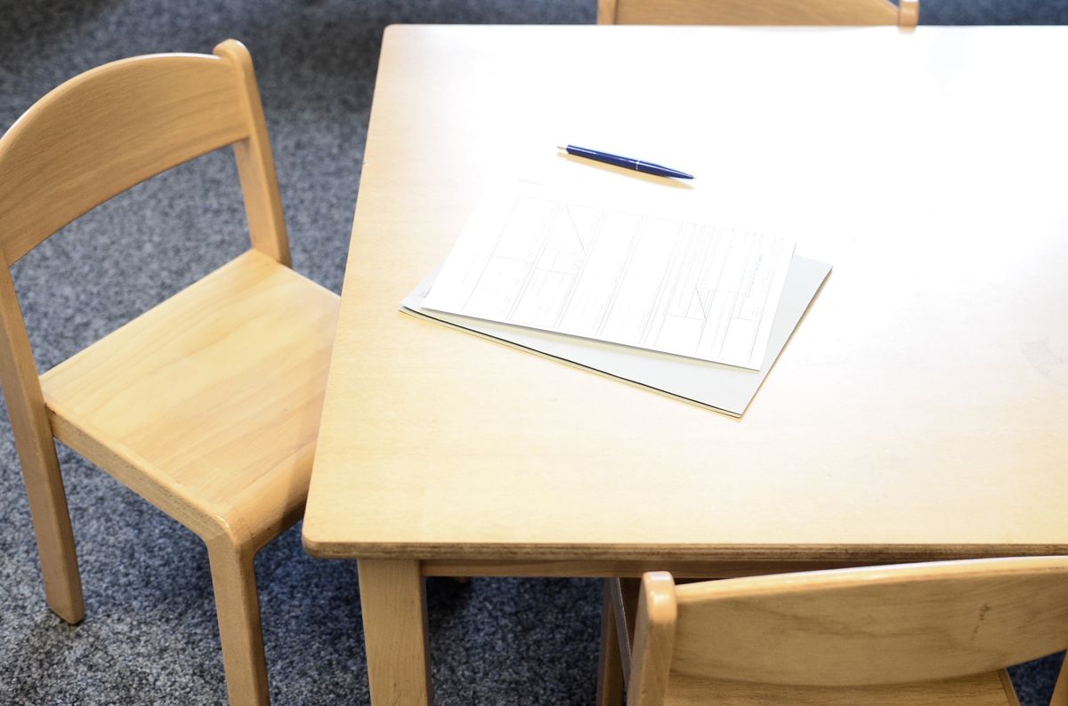 子ども用の低い木の机と椅子に、記入欄の並んだ用紙とボールペンが置かれている様子