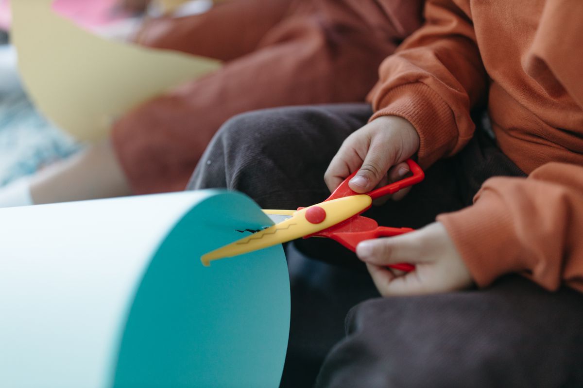 子ども用のはさみを両手で持ち、画用紙をぎこちなく切っている子どもの手元