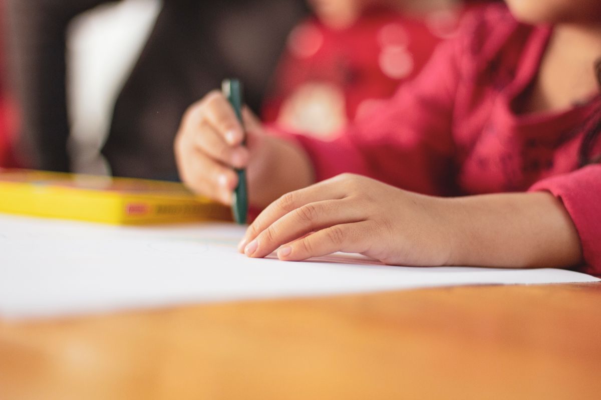 大きな白い紙の上で、子どもの手が緑のクレヨンを握っている。鉛筆と細い枠より、太い道具と広い面のほうが始めやすい