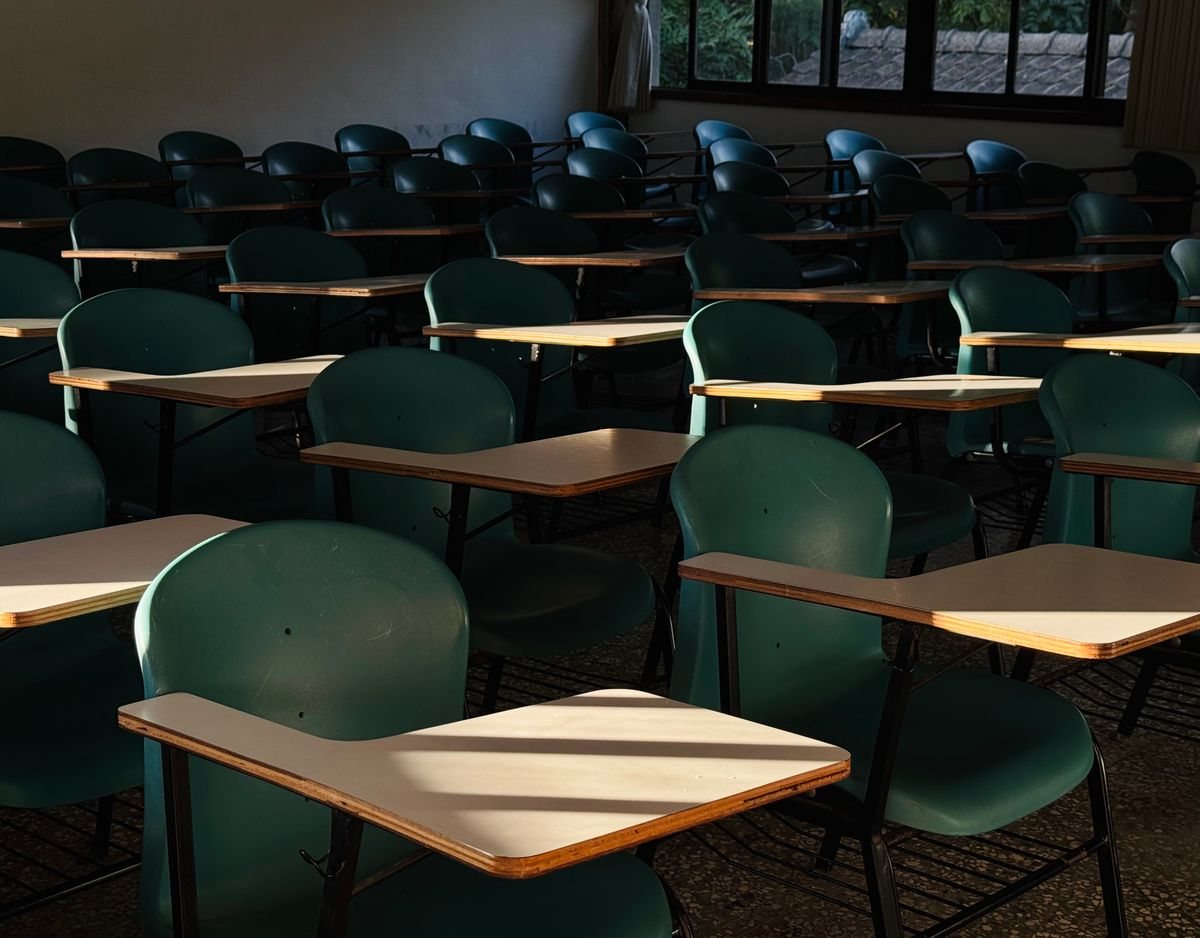 窓から差し込む光で机の天板が照らされている、誰もいない教室の緑の椅子の列。スクーリングの会場がどんな場所かを想像するイメージ