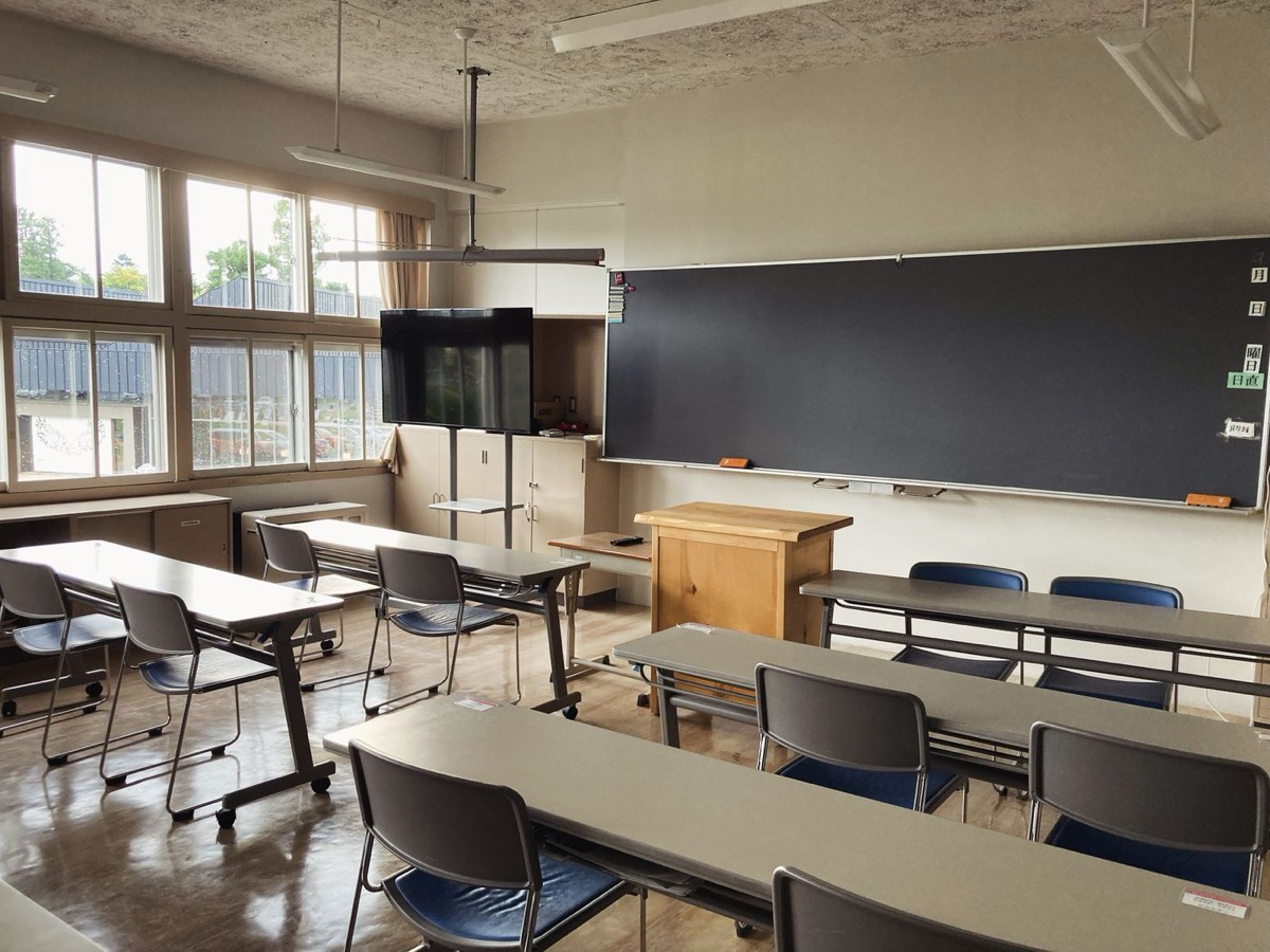 大きな窓から光が入る日本の学校の教室。黒板と教卓、可動式の机と椅子が並ぶ。学びの場を比べるときは、部屋の広さや人数の規模も見ておきたい