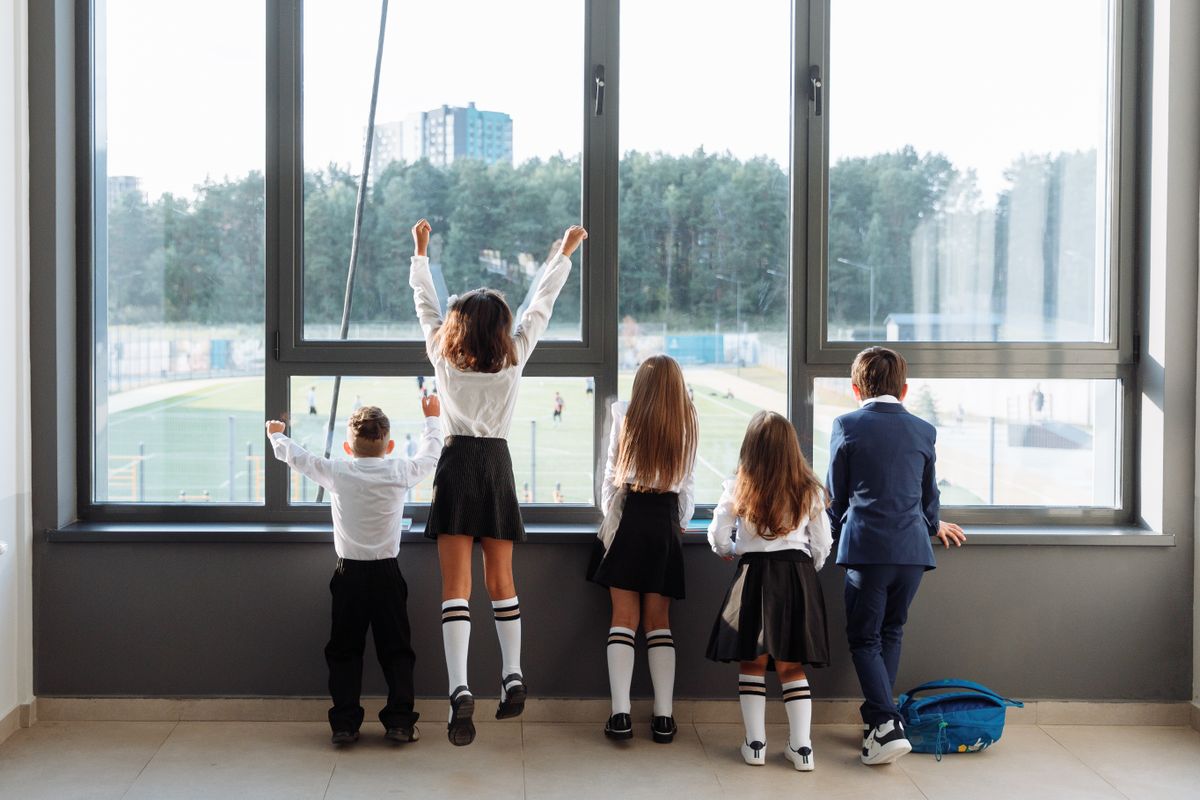 教室の大きな窓辺に並んで外をながめる小学生たちの後ろ姿。集団の中では一人ひとりの困りごとが外から見えにくい、というイメージ