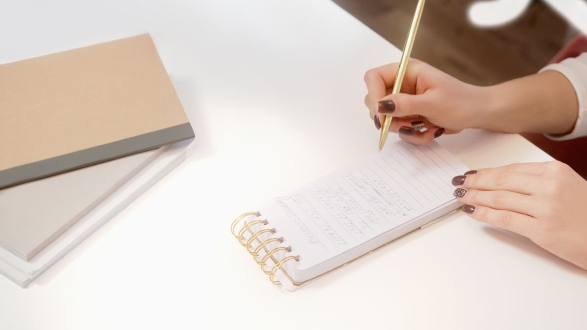 白い机の上で、らせん綴じのメモ帳にペンで書き込んでいる大人の手元。個別相談で聞きたいことを書き出しておくイメージ