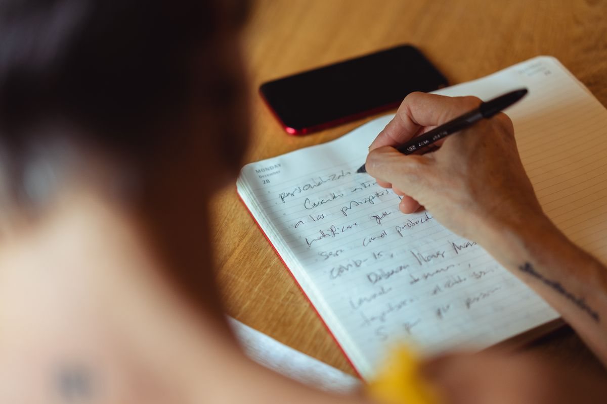 スマートフォンの横に置いたノートに、ペンで書き込んでいる手元。問い合わせ先を書き出して整理しているイメージ