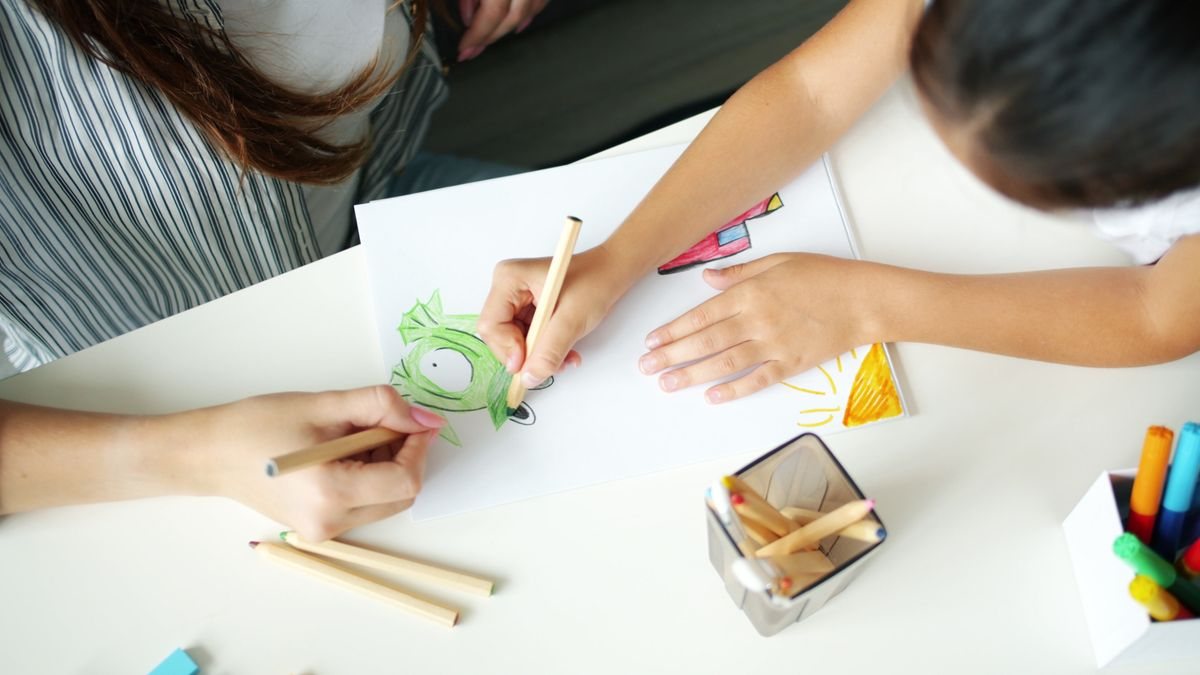 白い机の上で、大人と子どもが一緒に色鉛筆で絵を描いている手元