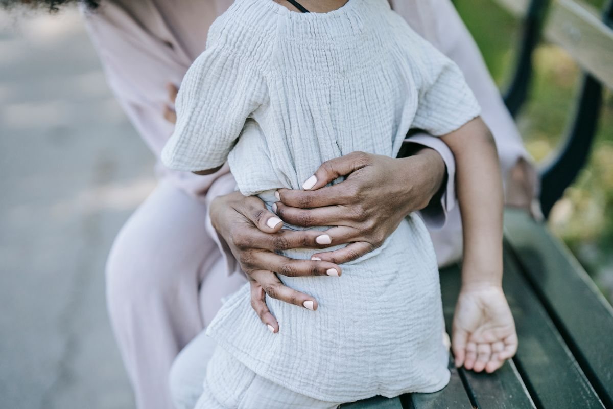 ベンチで大人の両手が子どもの背中を抱き寄せている手元。泣いた子を受け止めている場面のイメージ