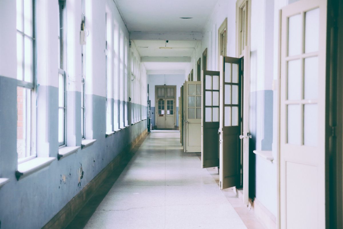 ドアが開いた明るく人けのない学校の廊下。授業の途中で教室を出て、別の部屋へ向かう場面のイメージ