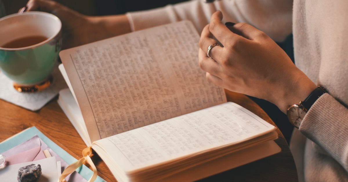 開いたノートに手書きで言葉をつづる手元と、温かいお茶のカップ。言葉にできない気持ちを紙に書き出してみる時間のイメージ